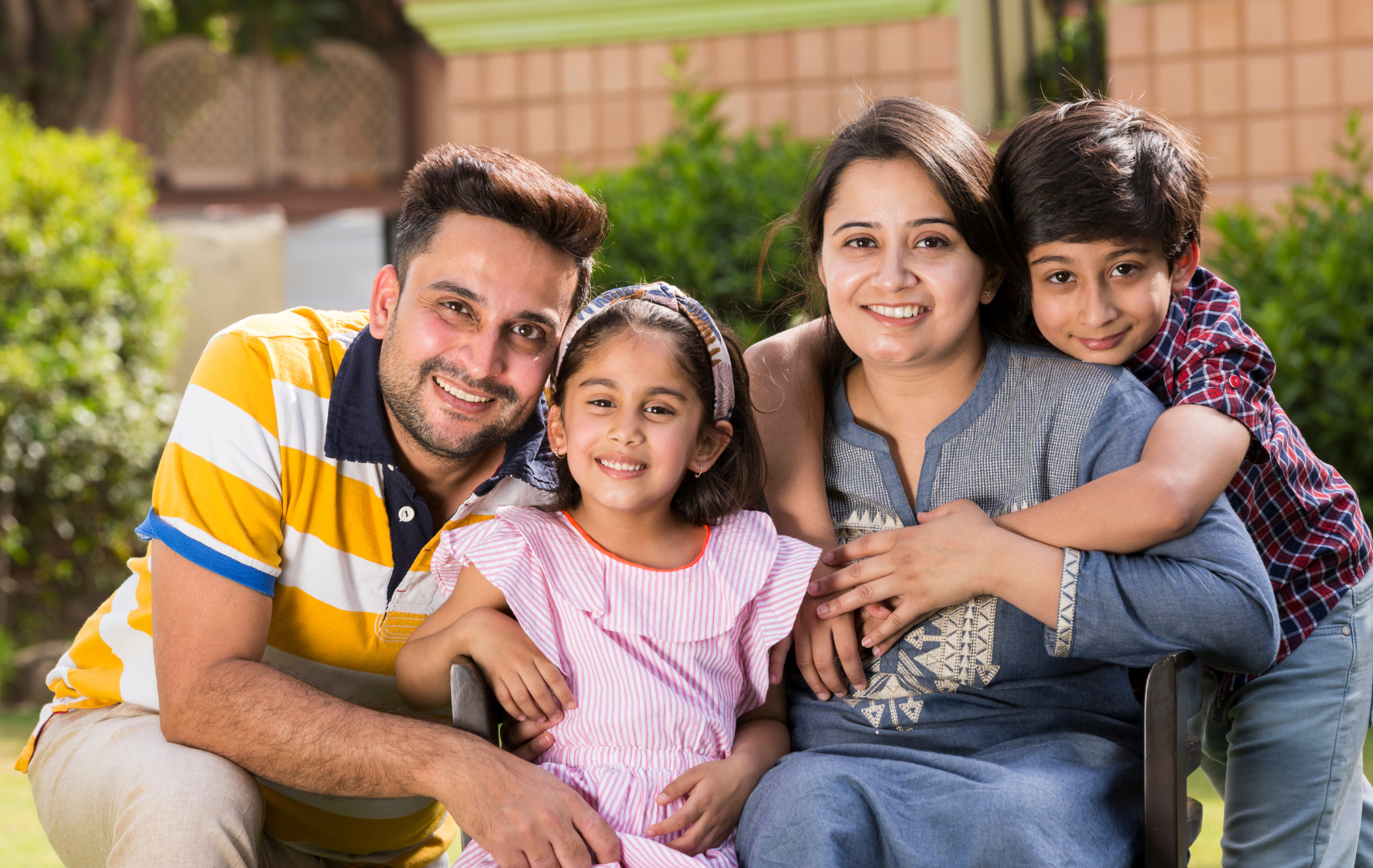 Happy Indian family portrait smiling outdoors in a bright, pleasant green garden setting.