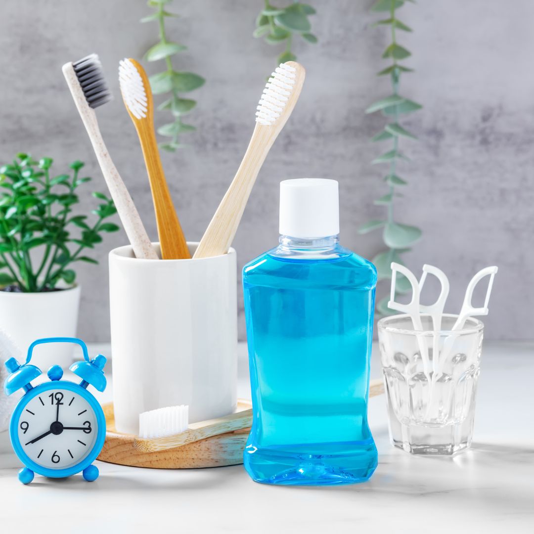 Oral hygiene essentials with bamboo toothbrushes, mouthwash, dental floss, and alarm clock on a bathroom counter.