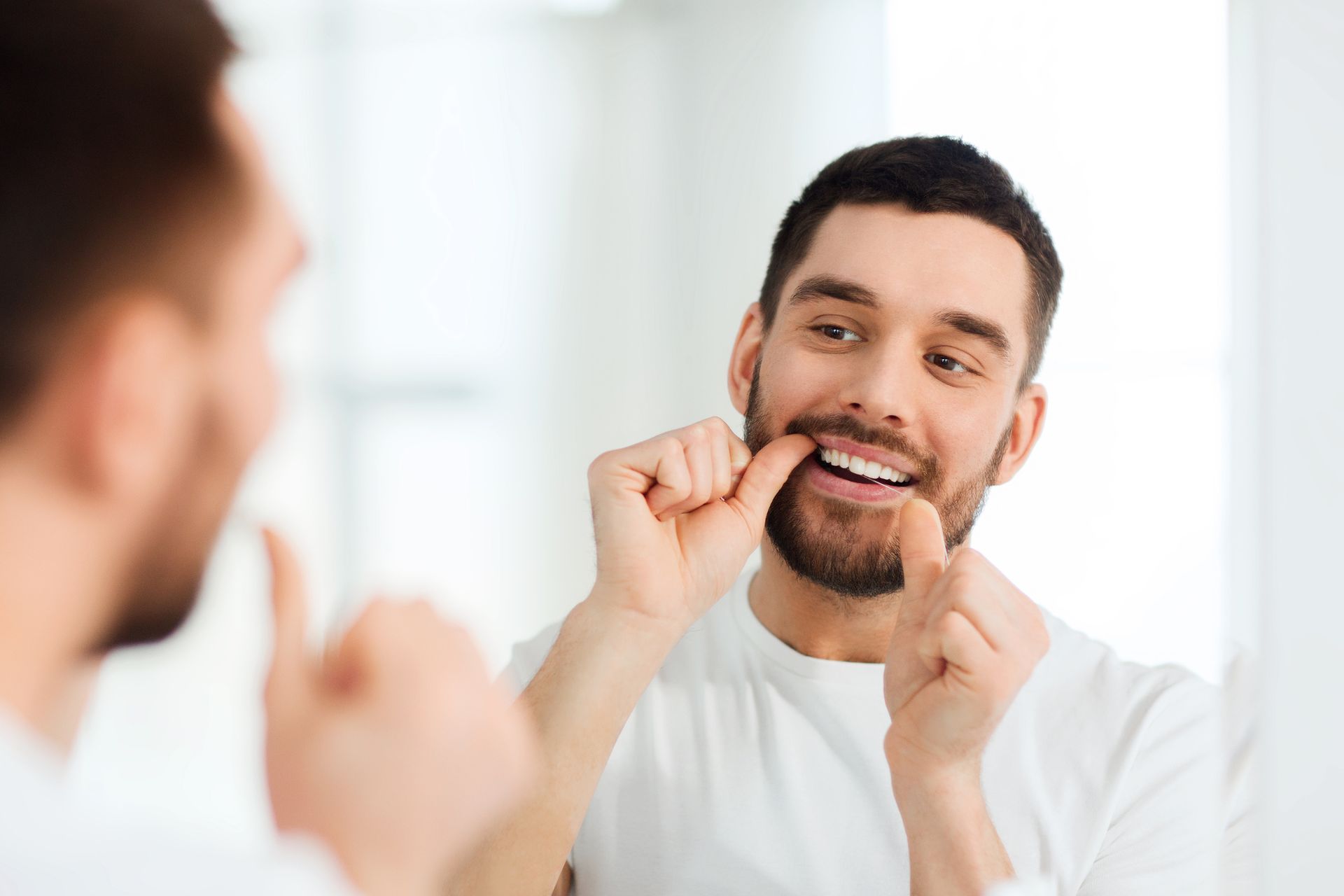 Man flossing his teeth in front of a mirror as part of daily oral hygiene routine.