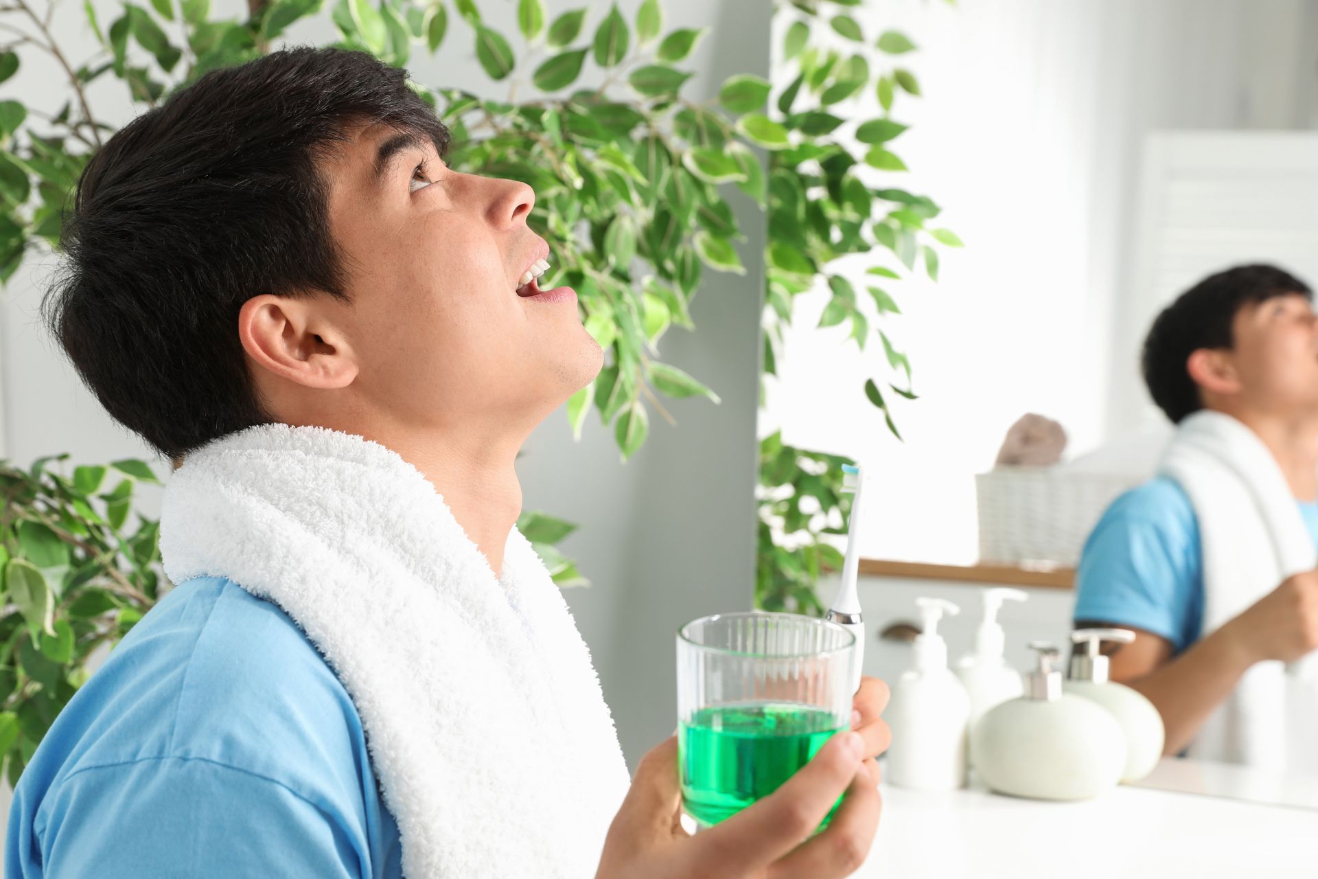Man rinsing his mouth with green mouthwash in bathroom mirror during daily oral hygiene routine.