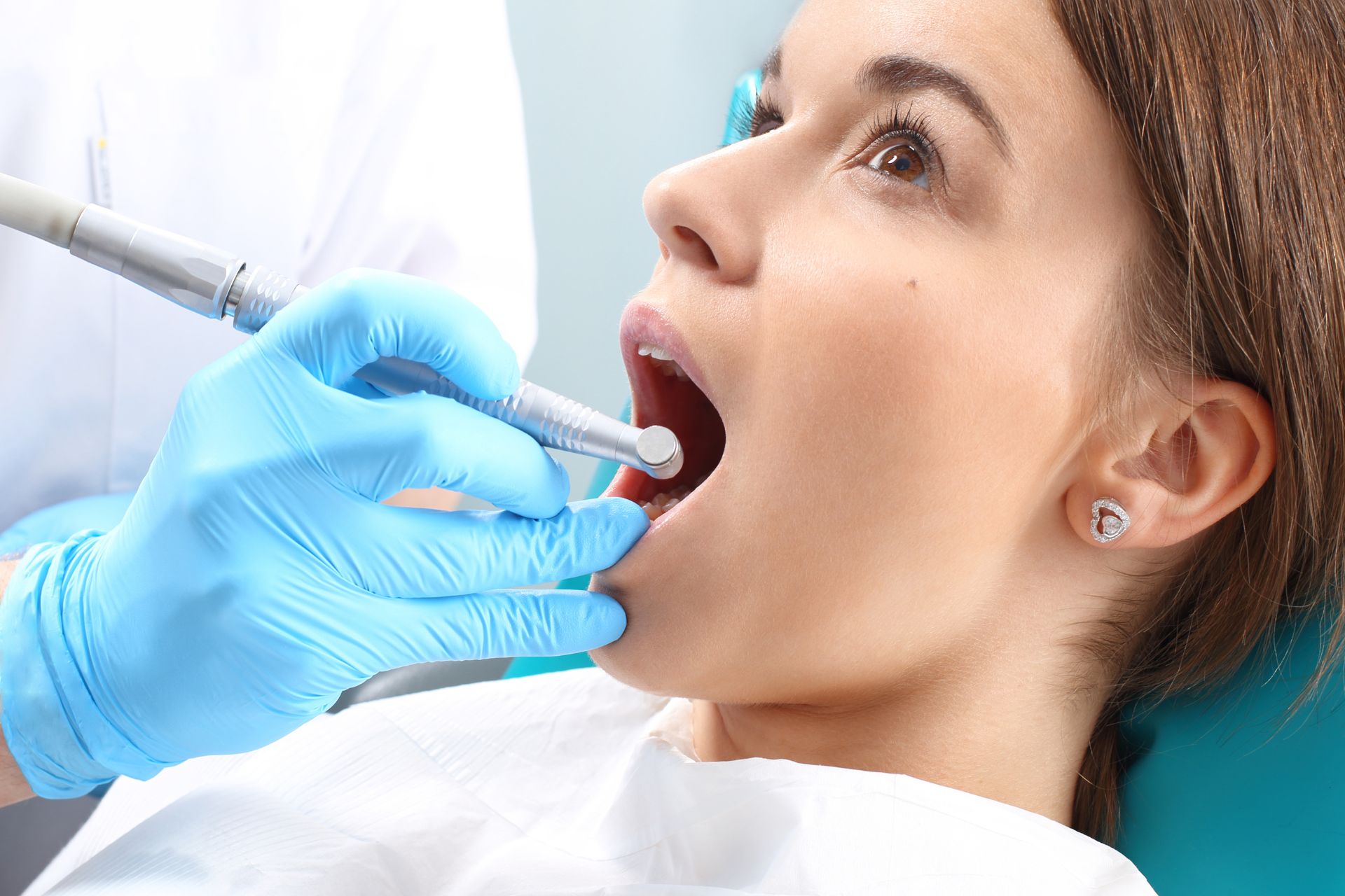 Dentist examining a woman’s teeth with dental drill during a routine oral check-up in a clinic.