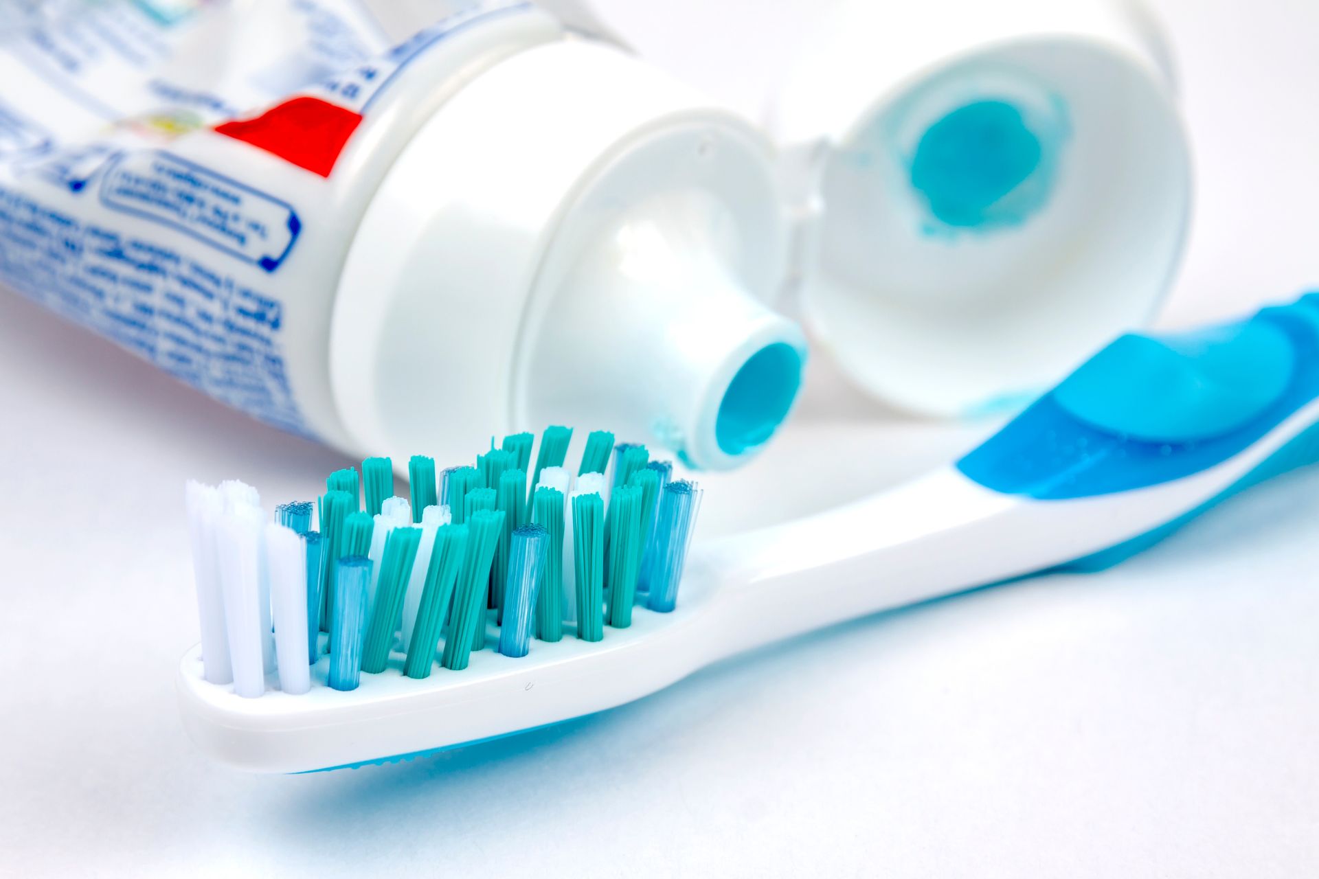 Close-up of toothbrush with blue bristles and toothpaste squeezed from tube on a white background.