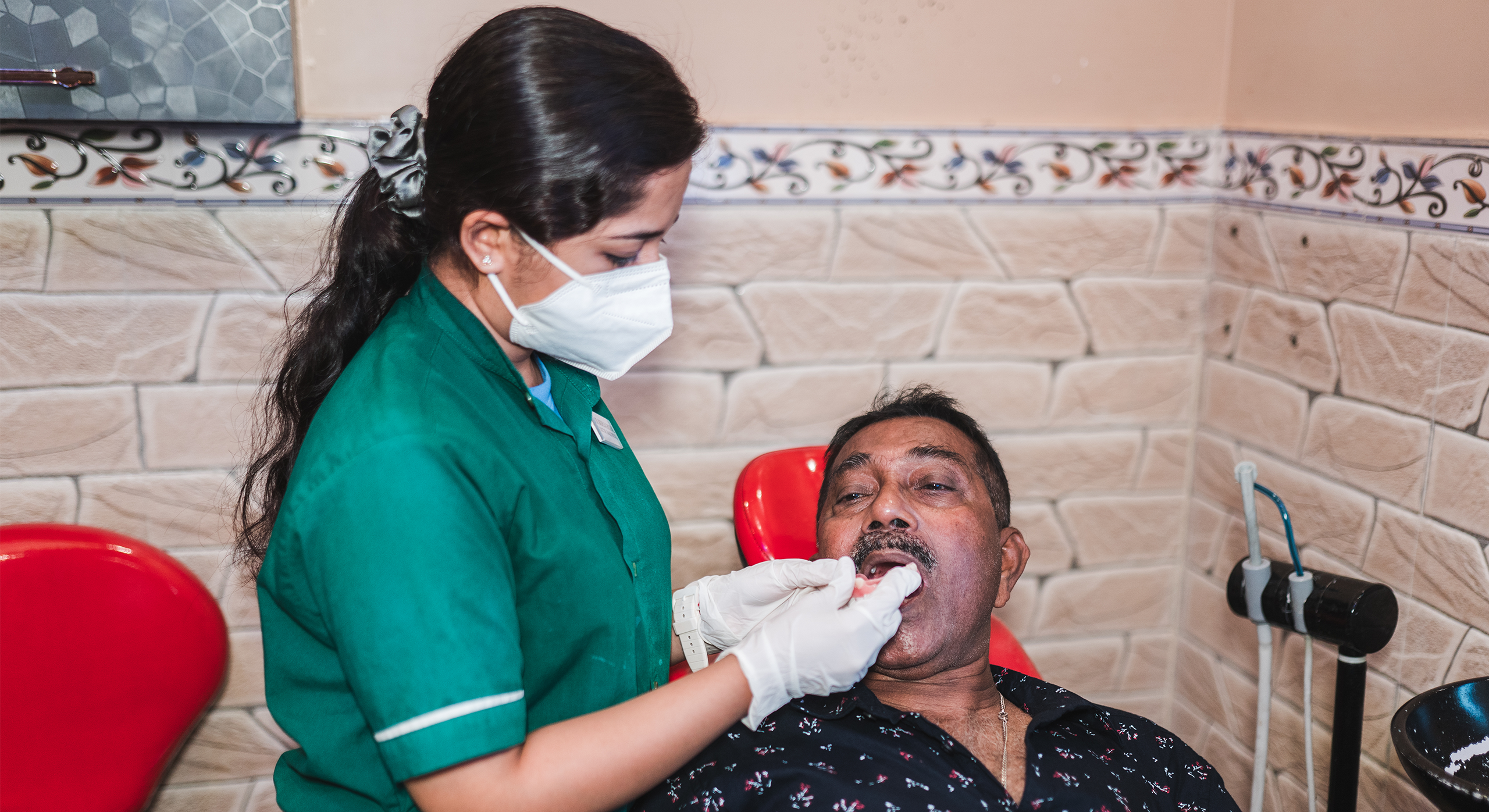 Dental assistant performing an oral check on an adult male patient seated in a treatment chair at a dental clinic.