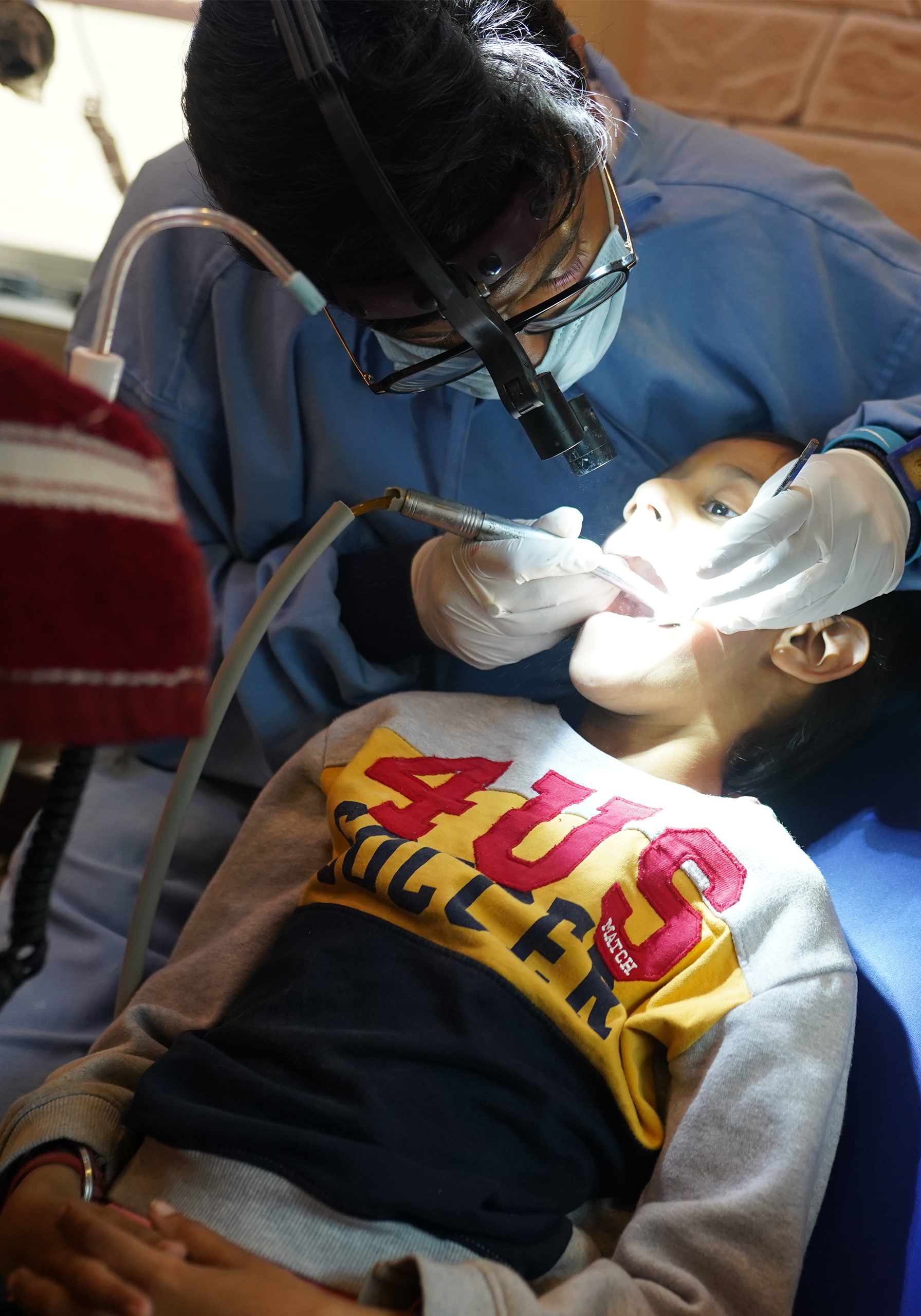 Dentist performing a pediatric dental procedure using focused lighting on a child in the clinic.
